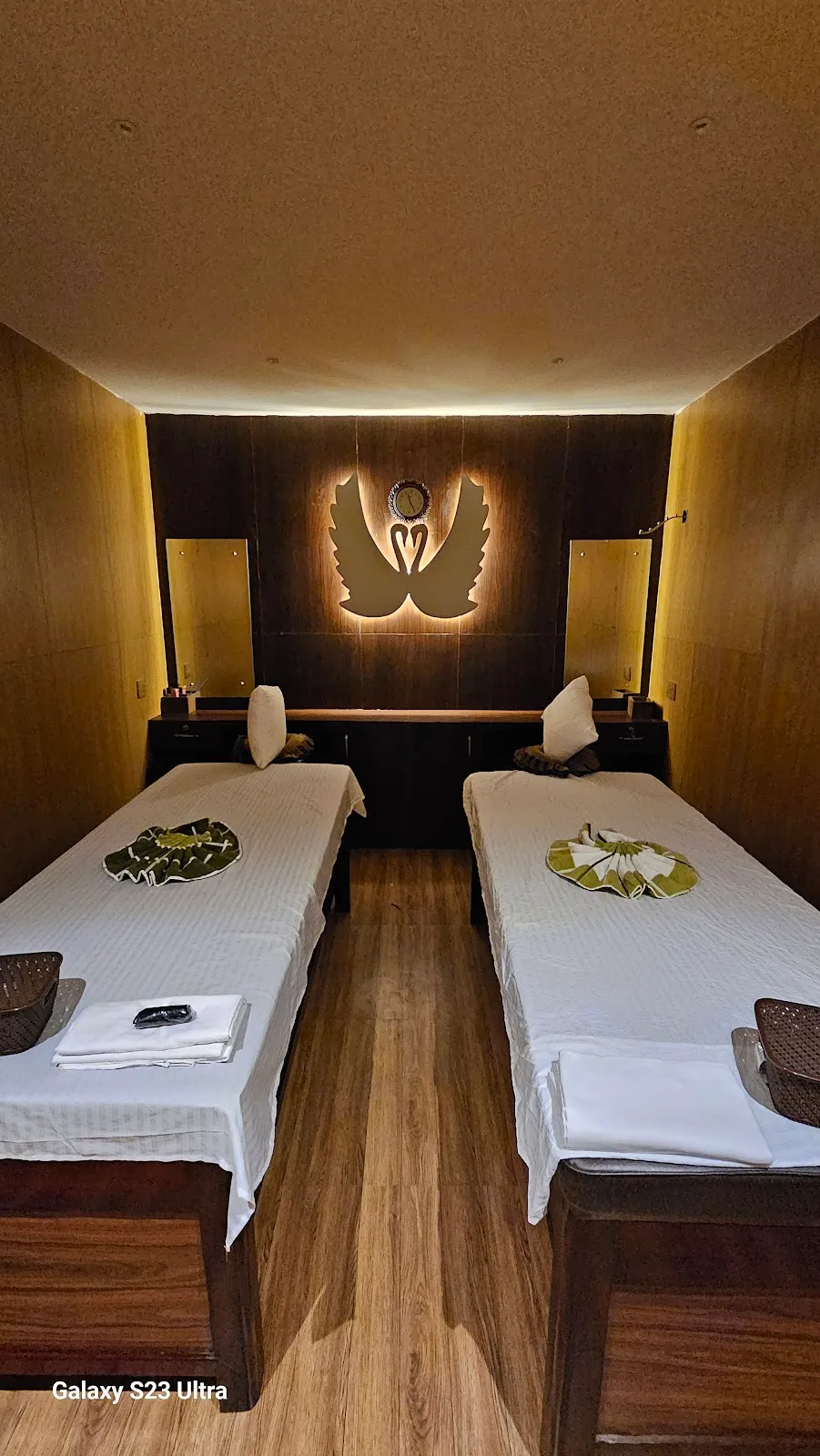 A softly lit twin-bed massage room at Paramount Spa Pokhara, with warm wood walls and an illuminated swan motif
